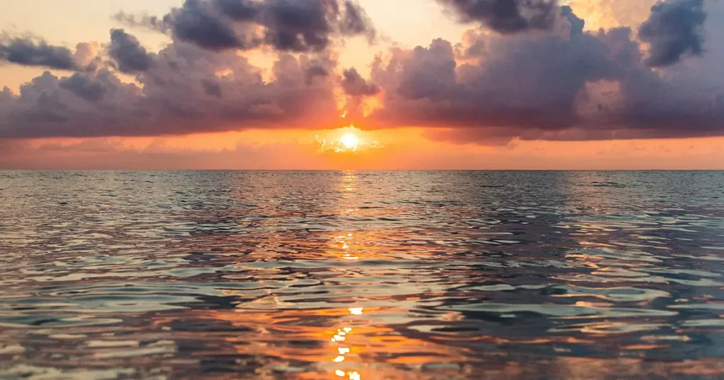 Lever de soleil sur l'océan avec eau en premier plan, symbolisant la transformation et la lumière émergeant de l'obscurité dans la reconstruction après trauma