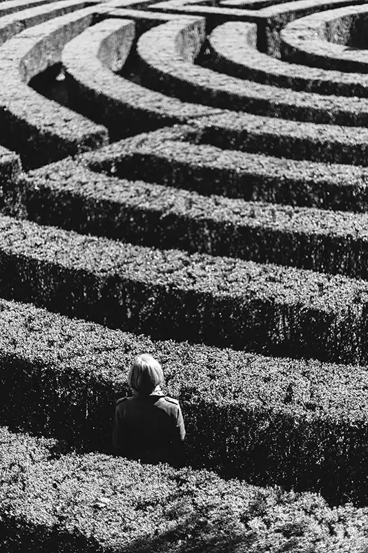 Femme seule face à un labyrinthe de haies en noir et blanc — symbole du chemin vers l'accomplissement de soi, hypnose authentique Touraine