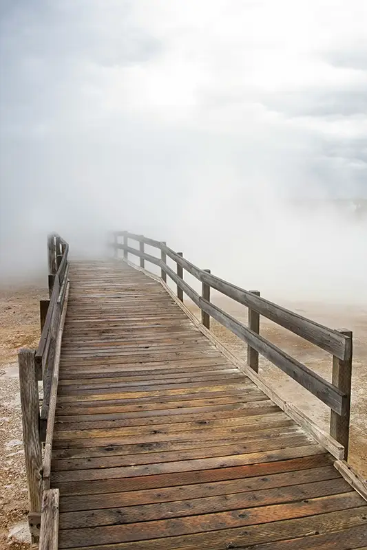 Passerelle en bois disparaissant dans la brume — image du passage vers l'état hypnotique, préparation à une séance d'hypnose en Touraine