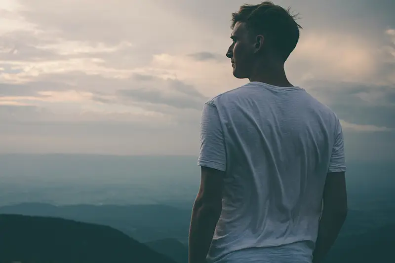 Homme de dos regardant un ciel nuageux depuis un sommet — se libérer de la mémoire traumatique et des manifestations somatiques, hypnose Touraine