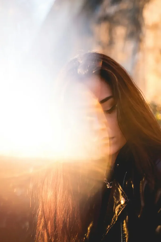 Femme regard baissé, visage dissous dans la lumière dorée — honte et culpabilité après une agression sexuelle