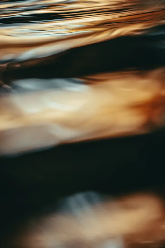 Surface d'eau floue en tons dorés et sombres — douleurs chroniques et mémoire somatique du corps