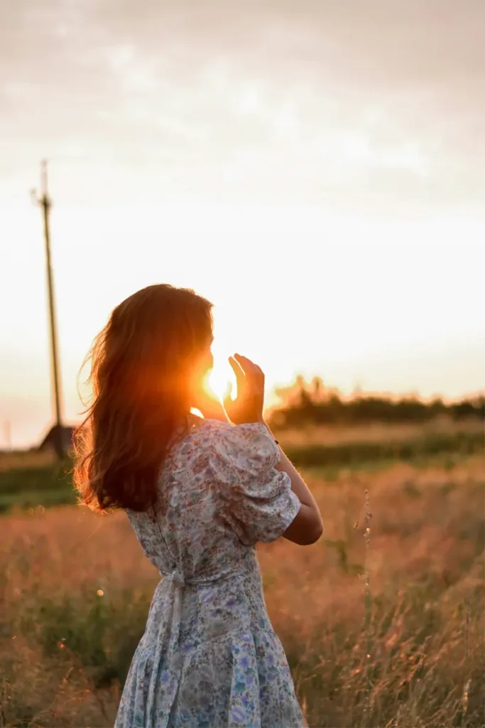 Femme de dos dans un champ au coucher du soleil, main levée vers la lumière — reconstruction de l'identité après violences sexuelles