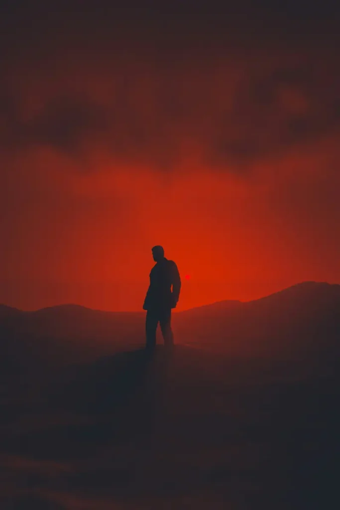 Silhouette debout sur une crête sous un ciel rouge sang — résilience et force intérieure après le traumatisme de guerre
