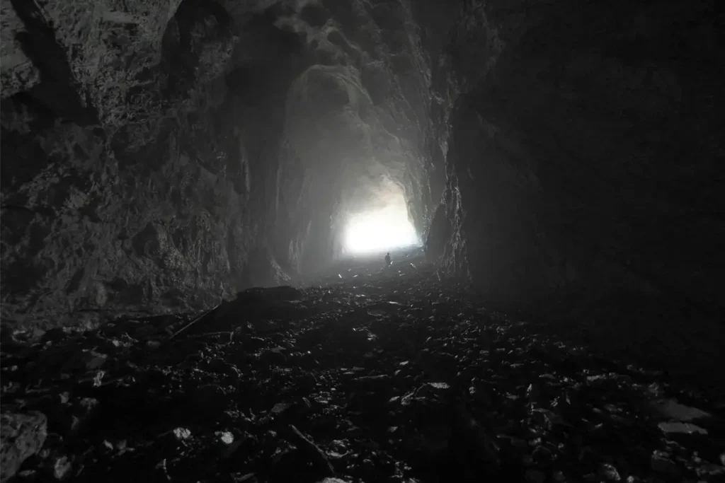 Grotte obscure avec silhouette humaine vers une lumière lointaine — le deuil comme descente et traversée psychique