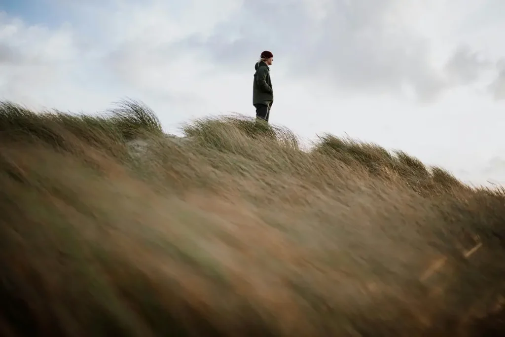 Silhouette debout sur une dune herbeuse sous un ciel nuageux, illustrant l'hypervigilance post-traumatique