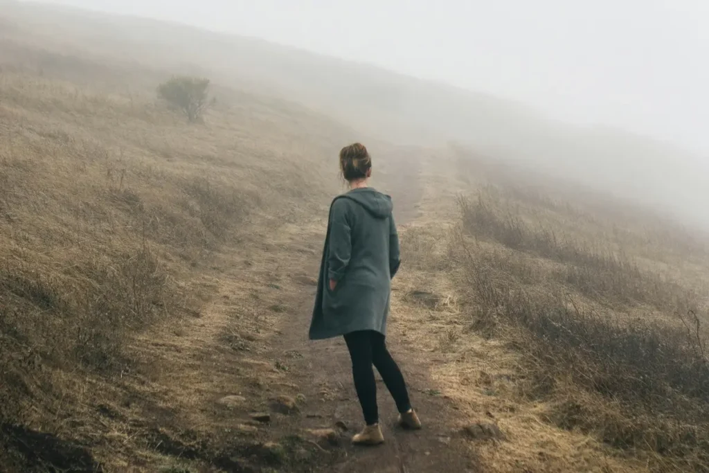 Silhouette de dos montant un chemin dans la brume, illustrant le processus de dénouement après un trauma résiduel