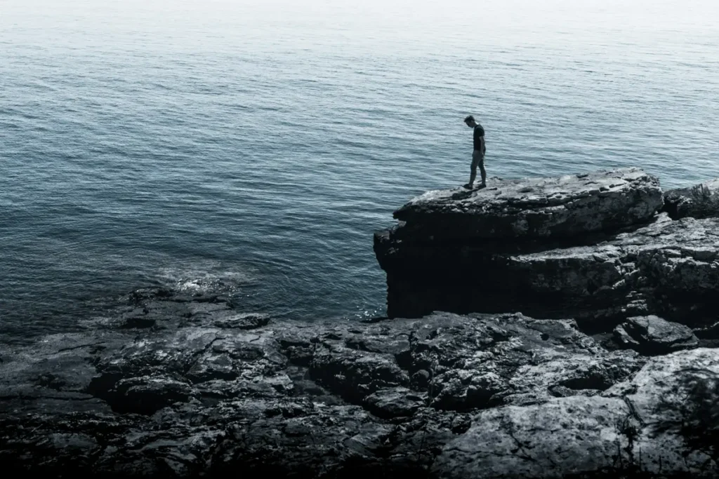 Silhouette debout sur un rocher face à la mer brumeuse, illustrant la mémoire corporelle du trauma résiduel