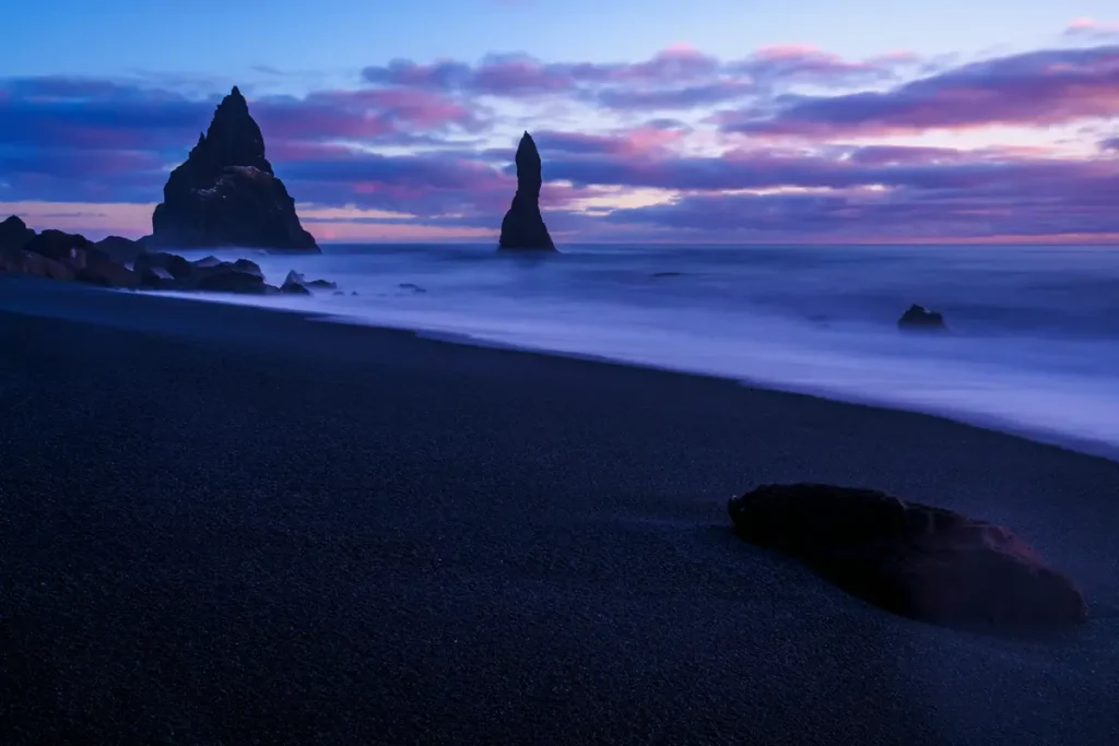 Plage de sable noir avec deux aiguilles rocheuses isolées face à l'océan au crépuscule, hypnose spécialisée pour le deuil à distance en expatriation