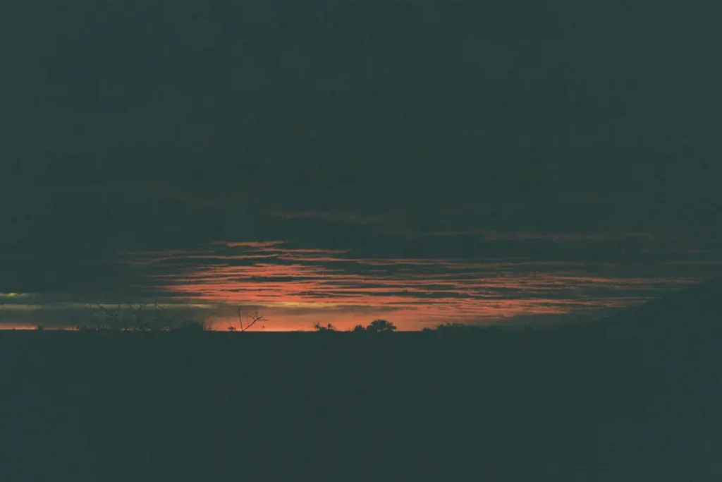 Fine bande de lumière orange à l'horizon d'un champ sombre au grain de pellicule, hypnose spécialisée pour l'isolement diffus en expatriation