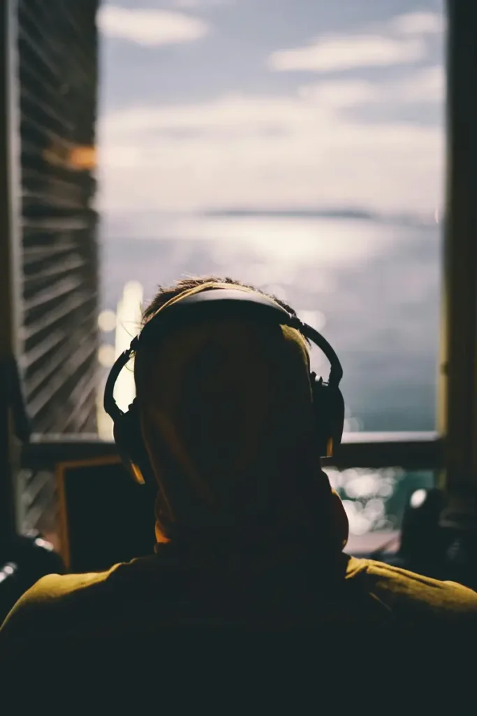 Personne de dos avec un casque, regardant par une fenêtre vers l'horizon, illustrant l'écoute à distance en hypnothérapie