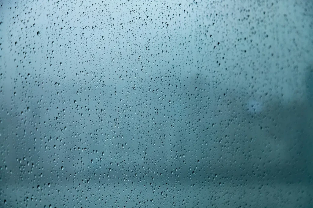 Gouttes de pluie sur une vitre floutant un arrière-plan bleu-gris abstrait, hypnose spécialisée pour l'expatriation de proximité