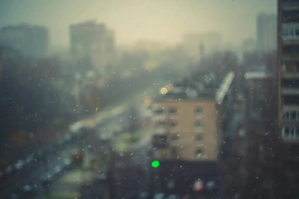 Toits urbains ternes derrière une vitre de pluie avec un point de lumière verte, hypnose spécialisée pour le personnel des organisations basées à Genève