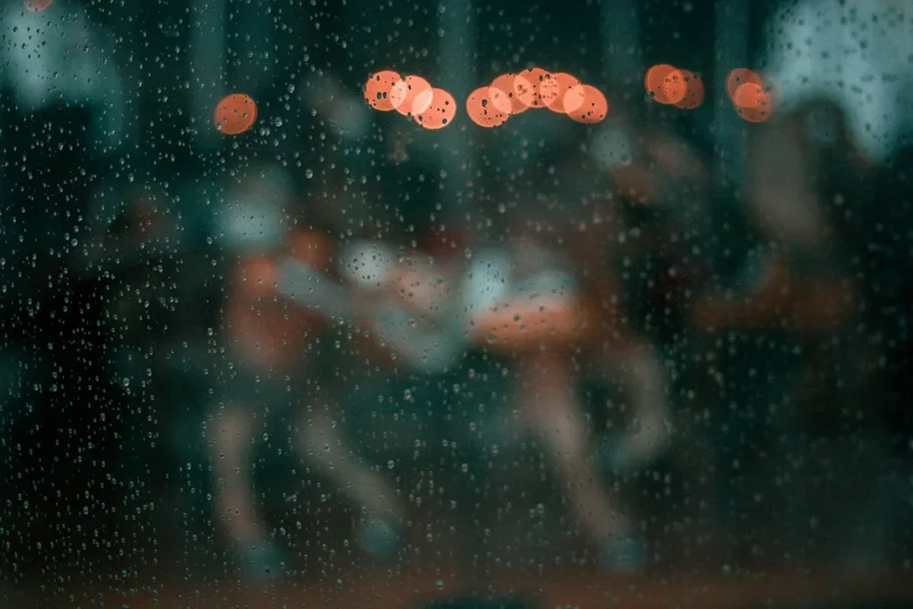 Silhouettes floues et lumières orange derrière une vitre de pluie, hypnose spécialisée pour l'incertitude professionnelle à Bruxelles