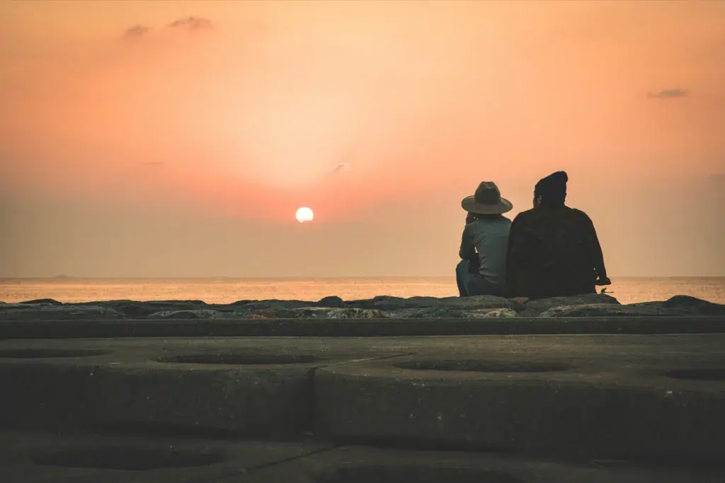 Couple assis séparément sur des rochers face à la mer au crépuscule